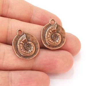 May include: Two copper-colored metal charms in the shape of a nautilus shell. The charms have a hole at the top for attaching to a necklace or bracelet.