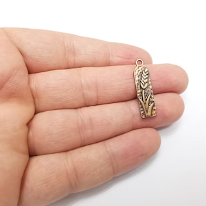 May include: A gold-toned metal charm with a wheat stalk design. The charm is about 2 inches long and has a loop at the top for attaching to a necklace or bracelet.