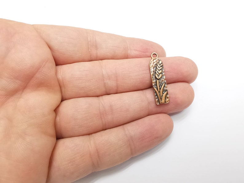 May include: A gold-toned metal charm with a wheat stalk design. The charm is about 2 inches long and has a loop at the top for attaching to a necklace or bracelet.