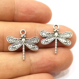 Könnte beinhalten: Zwei silberne Libellen-Anhänger mit filigranen Details. Die Anhänger haben oben eine Öse zum Anbringen an Schmuck oder andere Bastelarbeiten.