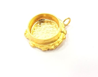 May include: A gold-colored pendant setting with a round, open bezel and a decorative, scalloped edge. The pendant has a small loop for attaching to a chain or cord. The setting is designed to hold a cabochon or other decorative element.