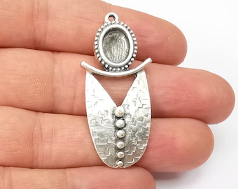 May include: Silver pendant with a textured oval shape and a round bezel setting. The pendant has a decorative design with a small, raised circle in the center.