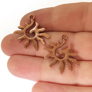 Peut inclure: Deux pendentifs en forme de soleil en cuivre avec un motif en spirale. Les breloques sont sur un fond blanc.