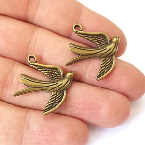 Peut inclure: Deux breloques d'oiseaux en métal doré antique avec un design détaillé. Les oiseaux sont en vol, les ailes déployées.