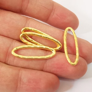 Pode incluir: Quatro anéis ovais de metal dourado com uma superfície texturizada. Os anéis estão empilhados uns sobre os outros.