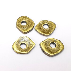 Puede incluir: Cuatro cuentas de metal de color dorado con forma cuadrada y un agujero en el centro. Las cuentas tienen una superficie texturizada.