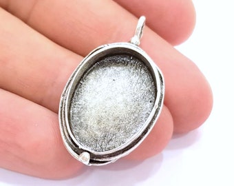 May include: Silver oval pendant setting with a smooth, slightly textured surface. The setting has a loop at the top for attaching a chain.