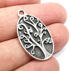 May include: Silver charm in the shape of an oval with a tree of life design. The tree has a detailed, intricate design with branches and leaves.