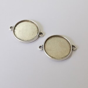 May include: Two silver-toned metal round pendant trays with a smooth, slightly textured surface. Each tray has two small loops on the side for attaching a chain or cord.