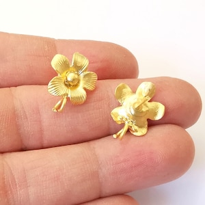 May include: A pair of gold flower-shaped stud earrings. The earrings have a textured surface and a small round center.