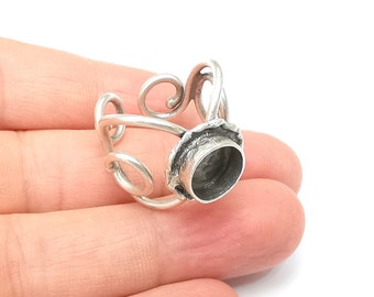 May include: Silver ring setting with a round bezel for a cabochon stone. The setting has a delicate, scroll-like design.
