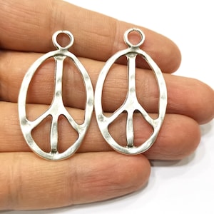 May include: Two silver peace sign charms with a textured finish. The charms are oval shaped and have a hole at the top for attaching to a necklace or bracelet.