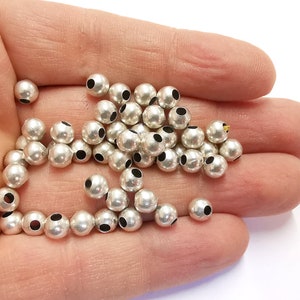 May include: A pile of silver metal beads with a hole in the centre of each bead. The beads are round and smooth.