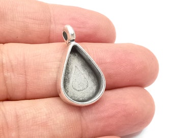 May include: Silver teardrop shaped pendant with a round opening for a cabochon. The pendant has a loop at the top for attaching a chain or cord.