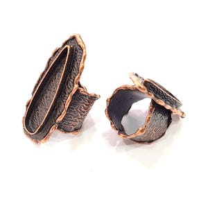 May include: Two copper rings with a textured, hammered finish. One ring is oval shaped with a smooth interior, while the other is a twisted band.