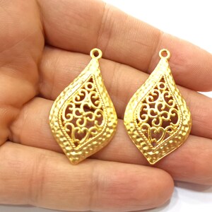 May include: Two gold-tone filigree pendant charms in the shape of a teardrop with a textured surface.