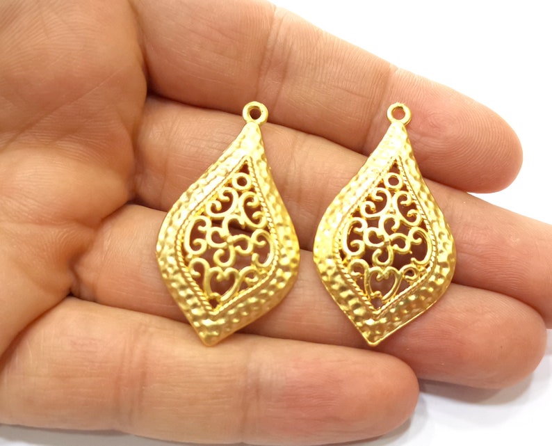 May include: Two gold-tone filigree pendant charms in the shape of a teardrop with a textured surface.