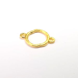Pode incluir: Conector de metal dourado com um design circular texturizado e dois pequenos laços. Este conector é ideal para a fabricação de joias.