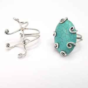 May include: Two silver rings with a turquoise stone. The ring on the left is a simple band with a decorative design. The ring on the right has a larger turquoise stone with a decorative silver design around it.