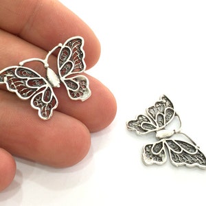 May include: Two silver filigree butterfly charms with intricate details. The charms are delicate and have a vintage aesthetic.