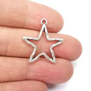 May include: Silver-toned metal star charm with a textured finish. The star is open and has a loop at the top for attaching to jewelry or crafts.