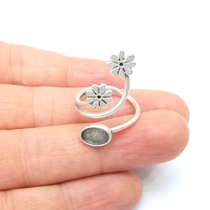 May include: Silver ring with a spiral design and two flower accents. The ring has a round, open space for adding a charm or stone.