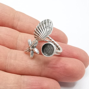 May include: Silver ring with a seashell and starfish design. The ring has a round bezel that can be used to hold a small photo or other memento.