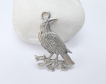 May include: Silver charm of a crow perched on a branch. The crow is detailed with textured feathers and has a realistic appearance.