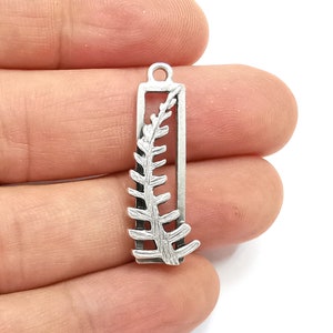 May include: Silver charm with a fern leaf design inside a rectangular frame.