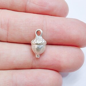 May include: A silver acorn charm with a loop at the top for attaching to jewelry or other crafts.