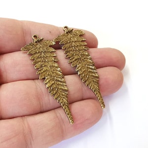 May include: Two gold-tone metal fern leaf charms with a loop at the top for attaching to jewelry or crafts.