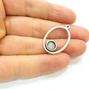 May include: Silver oval pendant with a smaller circle inside. The circle has a sparkly, textured surface.