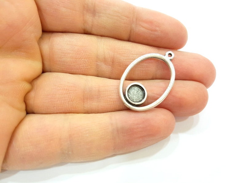 May include: Silver oval pendant with a smaller circle inside. The circle has a sparkly, textured surface.