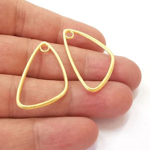 Puede incluir: Dos piezas en blanco para pendientes de metal de color dorado en forma de triángulo con un pequeño agujero en la parte superior de cada uno.