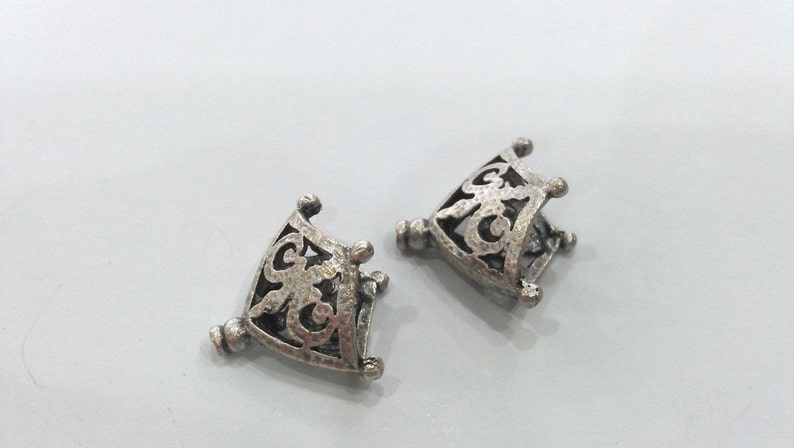 May include: Two silver-toned metal decorative pieces with an intricate, openwork design. Each piece is shaped like a square with rounded corners and has a delicate, floral pattern.