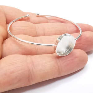May include: Silver bangle bracelet with a round, clear glass cabochon setting.