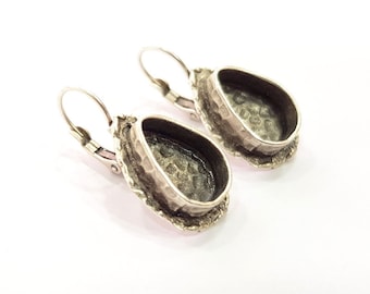 May include: A pair of silver teardrop-shaped earring settings with a textured surface. The settings are open on the top and have a hook closure.