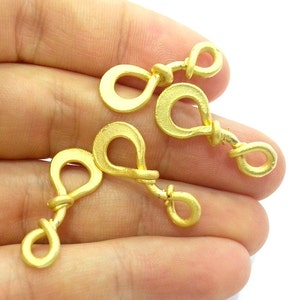 May include: Four gold-colored metal jewelry connectors with a twisted design. Each connector has two loops, one larger than the other.