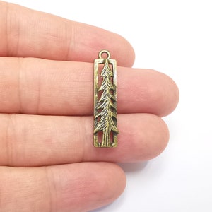 K&ouml;nnte beinhalten: Ein goldfarbener Metallanh&auml;nger in Form einer Tanne. Der Anh&auml;nger ist rechteckig und hat ein ausgeschnittenes Design einer Tanne. Der Anh&auml;nger hat oben eine Schlaufe zum Anbringen an einer Halskette oder einem Armband.