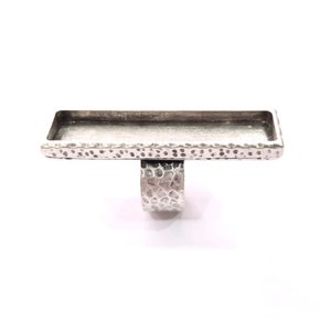 Pode incluir: Um anel de prata com uma bandeja retangular no topo. O anel e a bandeja têm uma textura martelada.