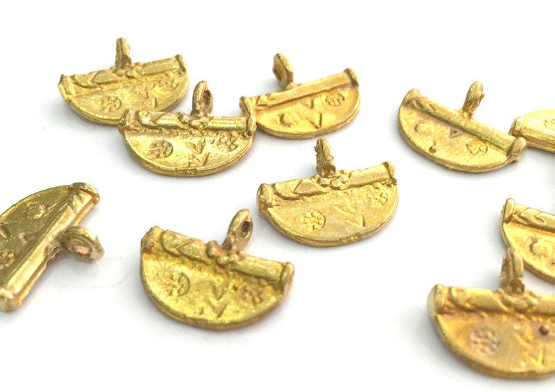 May include: A group of eight gold-toned metal charms with intricate designs. The charms are shaped like half circles and have a loop at the top for attaching to a necklace or bracelet.