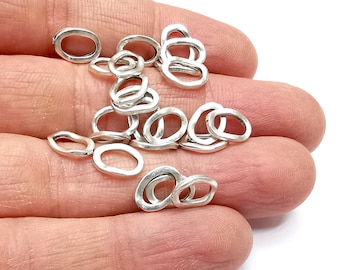 May include: A pile of silver jump rings, oval shaped, with a hammered texture. The rings are approximately 1/2 inch in diameter.