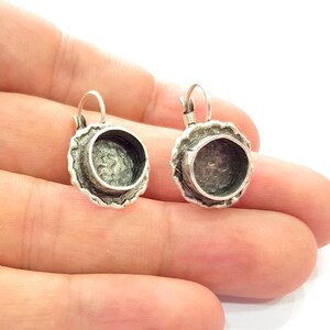 May include: Two silver-toned earrings with a textured, scalloped edge and a circular setting. The earrings have a lever-back closure. The earrings are shown against a light background.