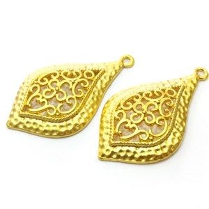 May include: Two gold-tone metal pendant charms with a filigree design. The charms are shaped like teardrops and have a textured surface.