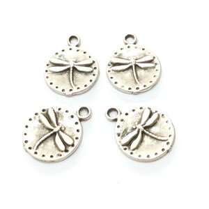 May include: Four silver-toned metal charms featuring a dragonfly design. Each charm has a loop for attaching to a necklace, bracelet, or other jewelry.
