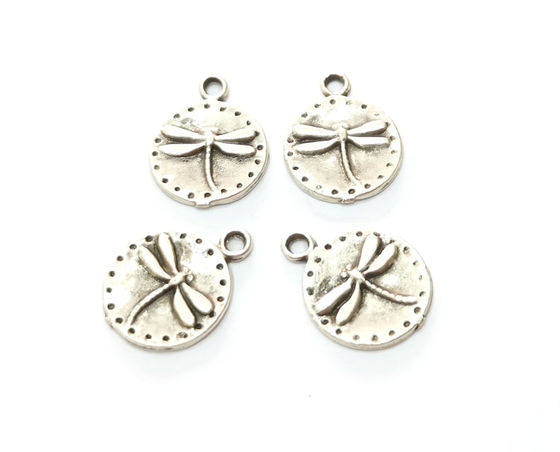 May include: Four silver-toned metal charms featuring a dragonfly design. Each charm has a loop for attaching to a necklace, bracelet, or other jewelry.