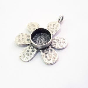 May include: Silver flower pendant with a round bezel for a cabochon. The flower has a hammered texture.