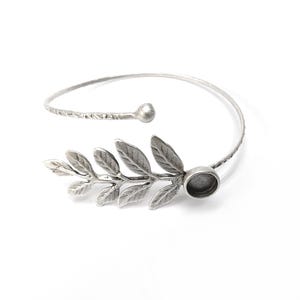 May include: Silver bracelet with a leaf design and a round, empty bezel for adding a charm or stone.