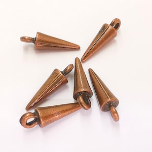 May include: Five copper-colored cone-shaped metal charms with a loop at the top. The charms are arranged in a star shape on a white surface.