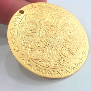 Peut inclure: Un pendentif en m&eacute;tal dor&eacute; avec un motif circulaire complexe. Le pendentif a un trou en haut pour l'accrocher.